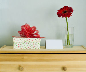 Red flowers in vase on table against wall