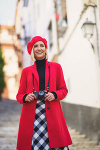 Woman with camera standing against building