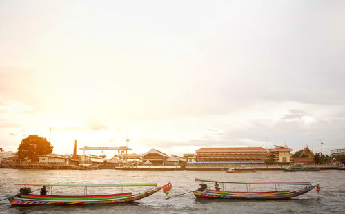 Boats moored in river against cloudy sky