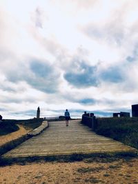 Rear view of people on road against cloudy sky