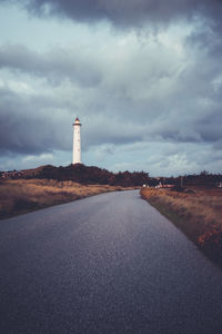 Lighthouse by road amidst buildings against sky
