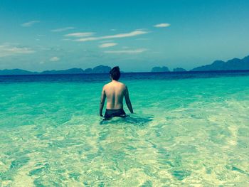 Rear view of shirtless man in sea against sky