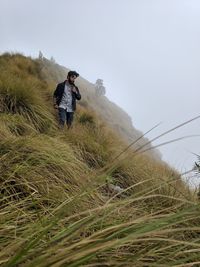 Low angle view of young man standing on grassy mountain against sky