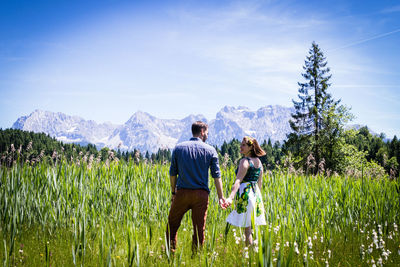 Rear view of friends standing on field against sky