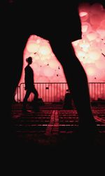 Silhouette people walking on illuminated road against sky at night