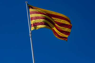 Close-up of the catalan flag flying in the blue sky.