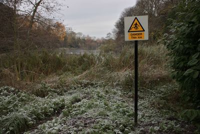 Road sign by trees on field against sky