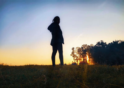 Silhouette woman standing on field against sky during sunset