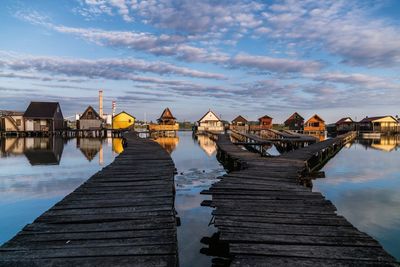 Scenic view of jetty leading towards beach huts against cloudy sky