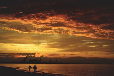 Silhouette people standing on beach against sky during sunset