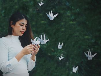 Young woman looking at paper bird against tree