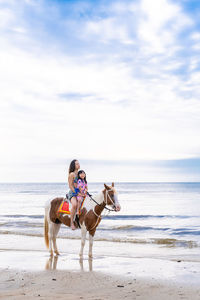 View of women and children ride horse on beach
