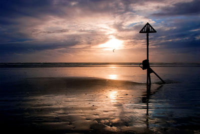 Silhouette structure on wet beach against cloudy sky during sunset