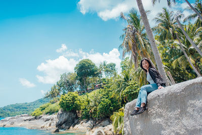 Man sitting on rock by sea against sky