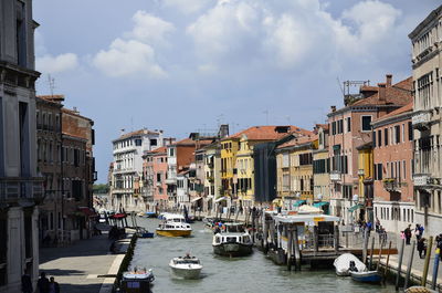 Sailboats moored on canal amidst buildings in city against sky