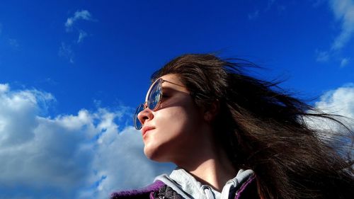 Low angle view of thoughtful young woman wearing sunglasses against blue sky