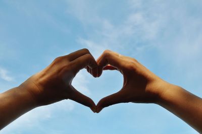 Cropped hands of woman making heart shape against sky