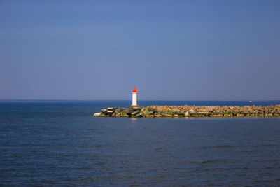 Lighthouse amidst sea and buildings against sky