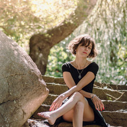 Young woman looking away while sitting on rock