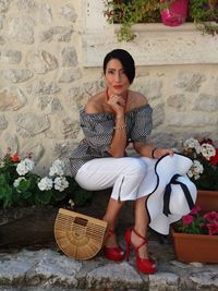 Portrait of young woman sitting by basket against wall