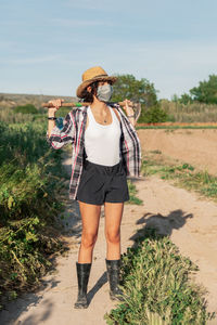 Farmer with axe wearing mask standing by plants against clear sky