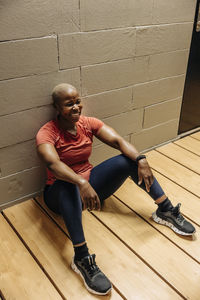 Happy female athlete taking break while sitting on floor at gym