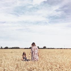 Mother and daughter on agricultural field against sky