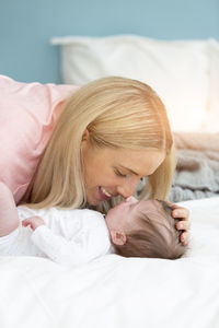 Mother playing with baby girl on bed at home