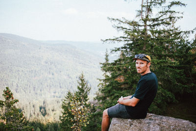 Portrait of man sitting on rock against mountains