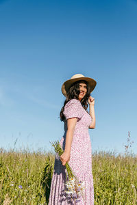 Beautiful woman standing in field, holding wildflowers