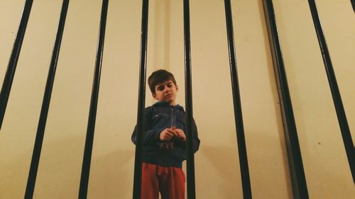 Boy standing against wall seen through railing