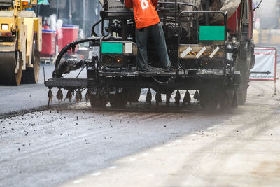 Low section of worker standing on construction vehicle at road