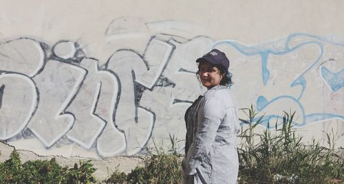 Side view of young man standing against graffiti wall