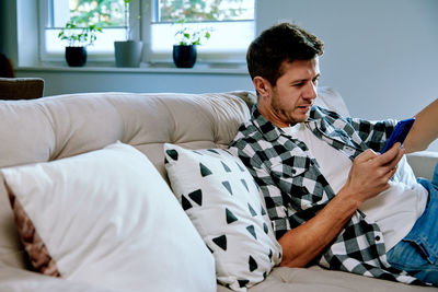 Man using smartphone while resting on sofa. online social media