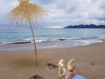 Low section of man wearing clogs at beach against sky