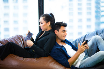 Colleagues using smart phones while relaxing on bean bag in office