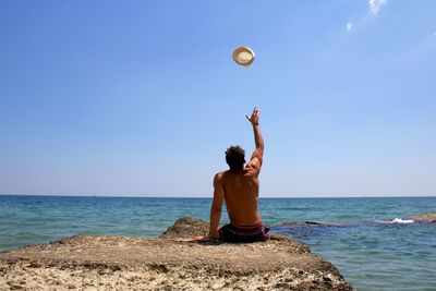 Rear view of shirtless man on beach against sky