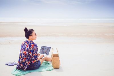 Woman sitting on shore at beach against sky