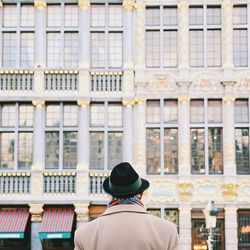 Rear view of man wearing hat while standing against modern building in city