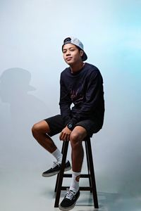 Young man looking away while sitting on seat against wall