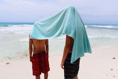 People with towel on face standing at beach against sky