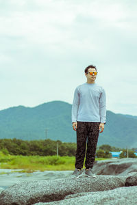 Portrait of young man standing on mountain against sky