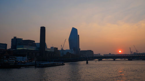 Scenic view of river by buildings against sky during sunset