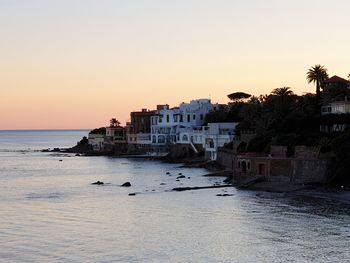 Sea and buildings against clear sky during sunset