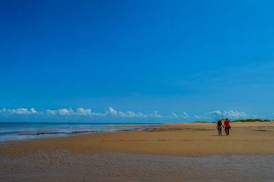 Couple walking at beach against blue sky