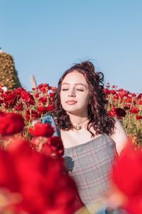 Beautiful young woman sitting amidst red poppy flowers against sky