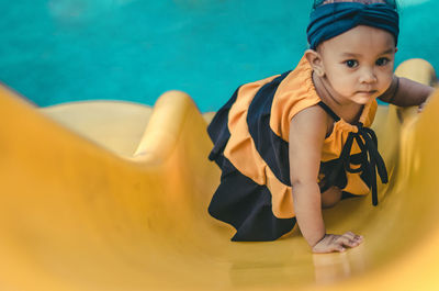 High angle portrait of baby girl on yellow slide at playground