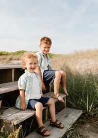 Portrait of smiling friends sitting on field against sky