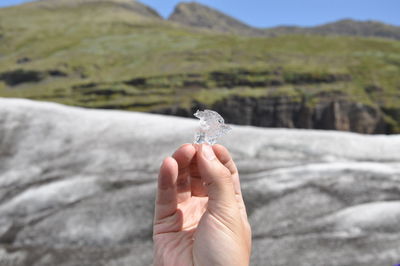 Close-up of human hand holding ice cube against mountains