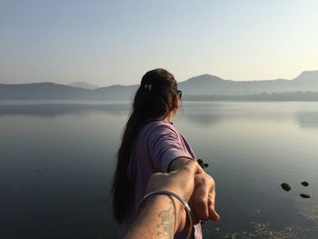 Cropped image of boyfriend holding girlfriend hand by lake